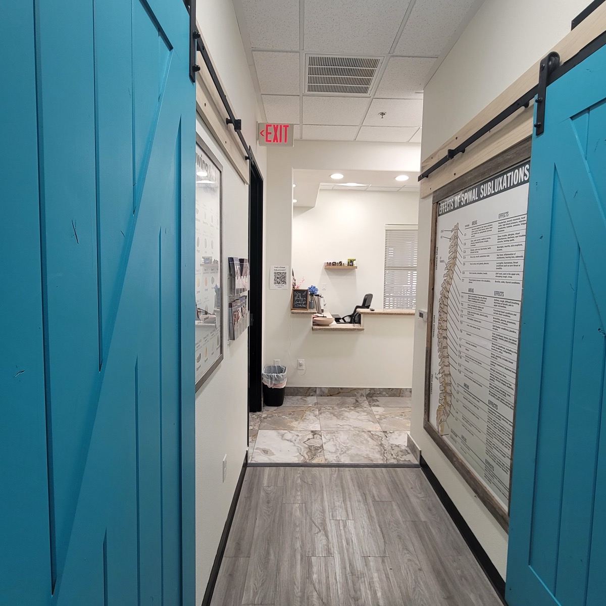 Hallway looking toward the front desk, with teal barn doors and a spinal chart at Evergrowth Chiropractic