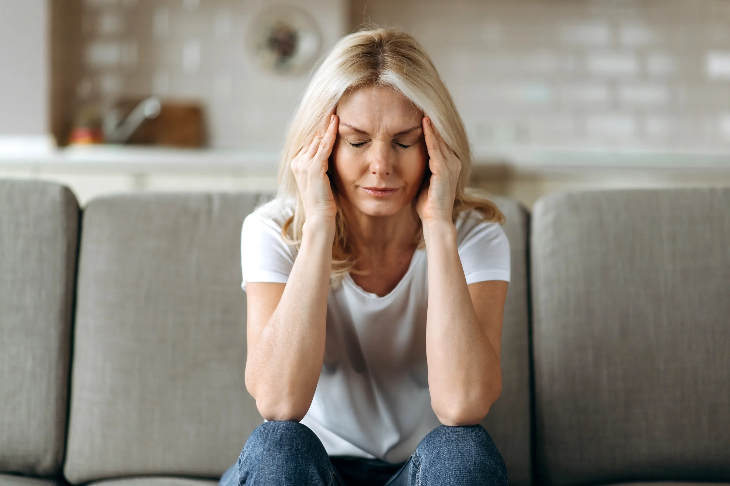 Woman sitting on a couch holding both sides of her head