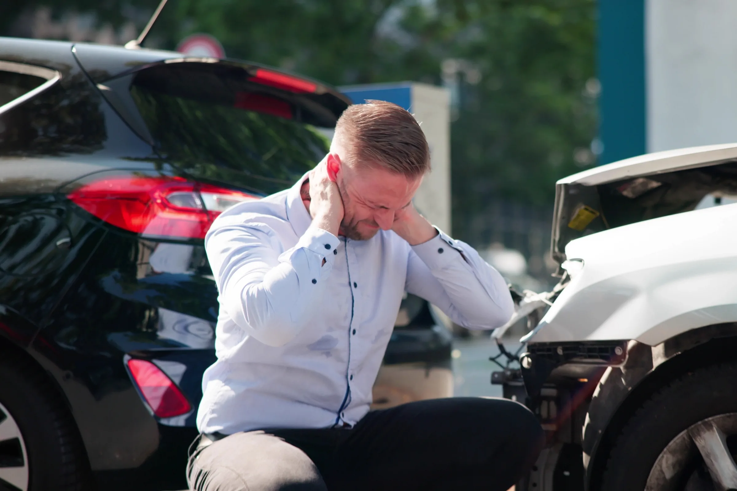 Man holding his neck between two damaged cars